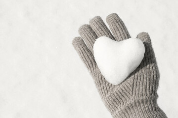 Female hand in brown glove holding heart shaped snowball, concept color of year 2026.