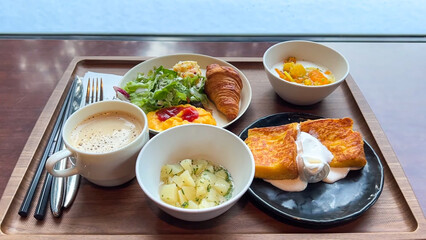 Luxury hotel breakfast set with French toast, croissant, scrambled eggs, salad and coffee served on a wooden tray