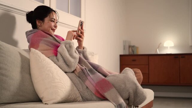 夜の暗い白熱灯のような灯りの部屋でストールを巻くスマホを持つ若い女性　女性の冬イメージ動画全身	