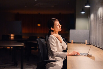 オフィスで暗くなるまで残業をして疲れる女性管理職