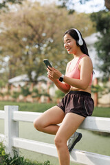 Young asian woman relaxing in park using smartphone and headphones