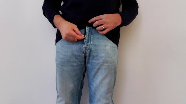 A subtle waistband grip moment as hands adjust light blue jeans against a dark sweater, capturing a quiet, intimate pause with soft texture and natural movement