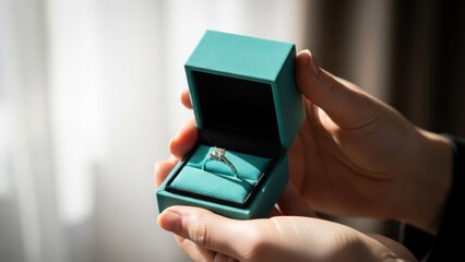 Close-up of a person holding a square, blue box containing a sparkling engagement ring
