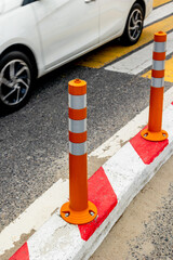 Traffic safety: orange bollard and white car on asphalt road
