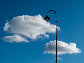 Obraz premium Dreamy blue skies meet vintage street lamp under fluffy white clouds on a sunny day for a whimsical feel, perfect for serene backgrounds