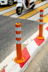 Urban crosswalk with orange traffic bollards and passing motorbike