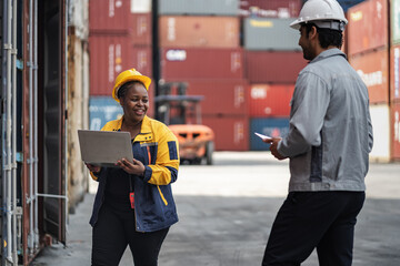 Man and woman logistics workers in high visibility safety gear discuss operations and checking container at shipping container yard	