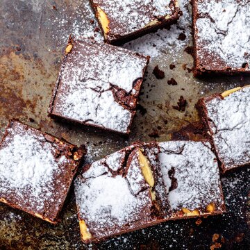 Chocolate brownies, dusted with powdered sugar, arranged on a dark metal surface