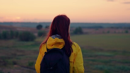 Lonely woman with backpack walks to empty farm field at sunset light. Woman traveler with backpack spend weekend in autumn park. Sportswoman on tour to wild nature at calm autumn evening twilight