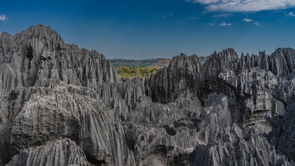 Black karst rocks with steep slopes and sharp peaks against a background of blue sky and clouds. ...