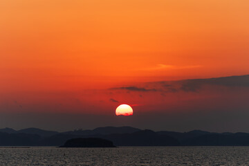Sunset Over the Sea with the Sun Veiled by Clouds and a Red Sky