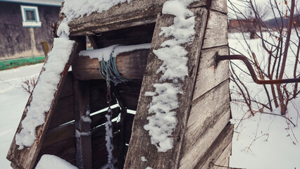 Old wooden well structure covered in snow in a winter landscape with bare trees and cold weather
