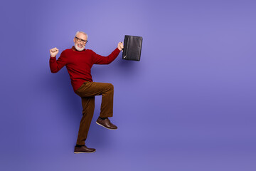 Happy mature man in a red sweater leaps with a briefcase against a purple background for stylish...