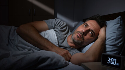 Man suffering from insomnia and difficulty sleeping at night. Middle-aged man awake in bed, staring blankly. Sleep disorder concept.