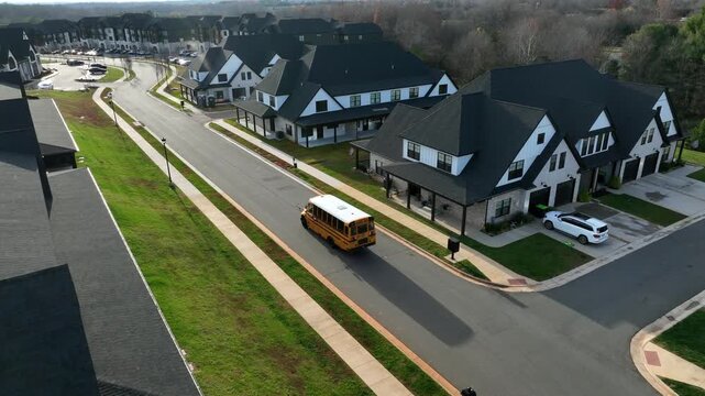 American luxury modern suburb with upscale homes, clean streets, dark gabled roofs and passing yellow school bus, surrounded by neat lawns in United States. aerial approaching shot.
