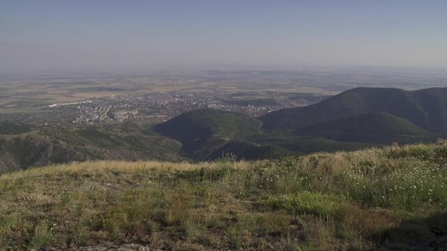 Breathtaking landscape shows a wide view from Stara Planina, looking down at Sliven valley and Sliven city below. The sun casts bright light over the hills, enhancing the beauty. Balkan Mountains.