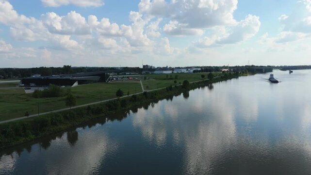 Drone pullback tilt up over Marshals Museum along calm Arkansas river reflecting museum and clouds in sky
