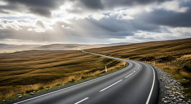 A winding asphalt road through rolling hills under a cloudy sky.