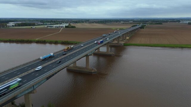 Aerial drone cinematic panorama of River Trent crossing near Goole Yorkshire UK with motorway bridge, vehicles and industrial transport infrastructure landscape
