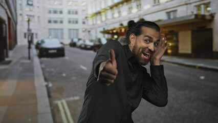 Man cupping ear with hand on busy city street near parked cars, wearing black shirt with beard; curiosity attentive.