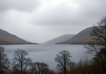 Misty mountains overlook a serene lake on an overcast day.