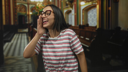 Young woman with hand to forehead and expressive grin wearing knotted striped shirt making a playful gesture in church building aisle; playful moment.