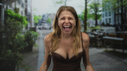 Obraz premium Woman screaming with hands clawing and cleavage visible on a city street lined with bicycles and planters, leaning forward; anger.
