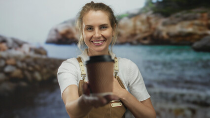 Woman smiling in apron with coffee cup by seaside beach under clear sky.