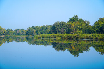 A small river or lake with blue water and a green forest on the shore under a blue sky. Summer landscape