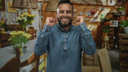 Fototapeta premium Man smiling with clenched fists beside yellow tulip bouquets in a rustic flower shop set in a studio building interior; joy.