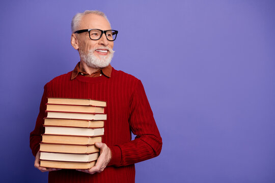 Senior man with glasses holding a stack of book smiles against a purple backdrop