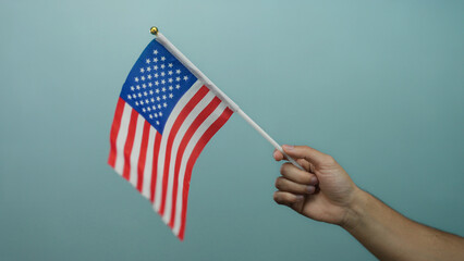 Man holding american flag against blue background signifies patriotism and national pride, emphasizing symbolic gesture with isolated backdrop.