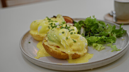 Brunch scene featuring eggs benedict with lush salad on a plate indoors at a restaurant highlighting fresh chives and creamy hollandaise sauce.