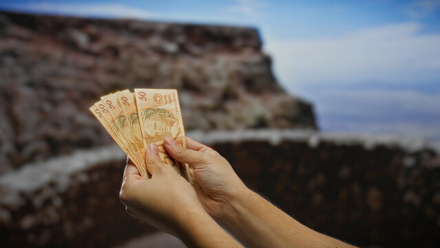 Man holding brazilian reais banknotes outdoors in an urban setting, showcasing currency handling and financial concepts on a city street.