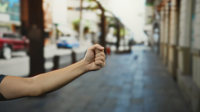 Man's hand clenched in a fist on a city street, symbolizing strength and determination, with urban landscape blurred in the background.