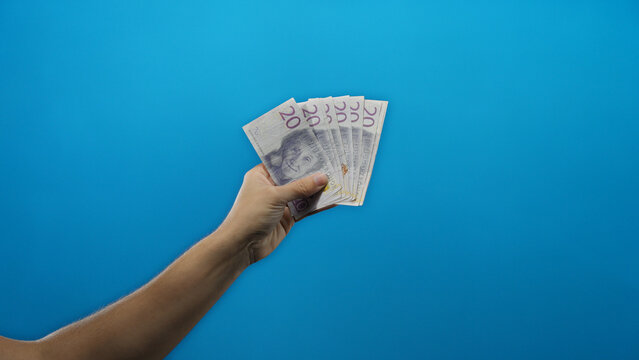 Man's hand holding swedish kronor banknotes in front of a vivid blue background, symbolizing financial concepts and currency exchange with a focus on sweden's economy.