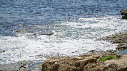 Serene mediterranean coastal scene with clear blue sea, sunlit waves breaking on rocky shore, showcasing nature's beauty during a sunny day outdoors.