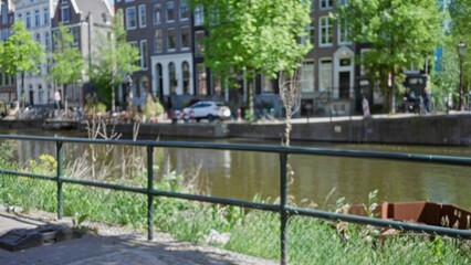 Blurred view of amsterdam canal with defocused buildings and greenery under bright sunlight...