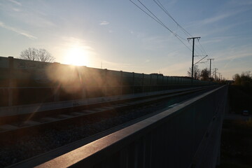 The sun is setting behind a fence and the sky is blue