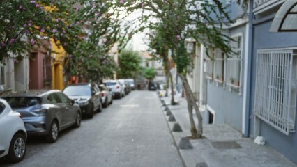 Fototapeta premium Narrow residential lane lined with parked cars and flowering trees, softly defocused bokeh street; background, copyspace, backplate.