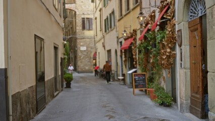 Fototapeta premium Narrow european alley with cafe storefronts and red awnings, softly blurred shallow bokeh alley; background backplate copyspace calm.