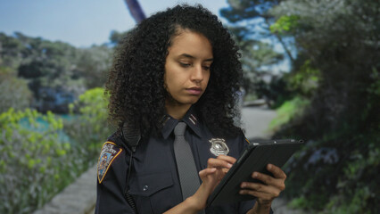 Woman police officer using tablet in outdoor park setting showcasing focus and professionalism