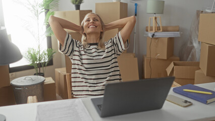 Woman sorting papers and handling documents with hands visible at desk, surrounded by moving boxes in building; relief accomplishment.