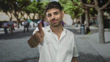 Naklejka premium Confident man makes vigorous thumbs up gesture with bare thumb on street amid blurred pedestrians; approval.