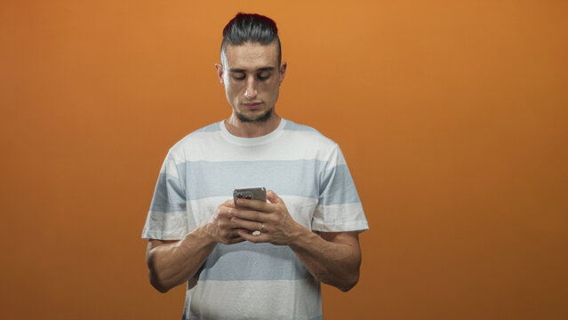 Man tapping smartphone and giving thumbs up gesture in studio orange backdrop, looking at phone; joy connection engagement. - Powered by Adobe