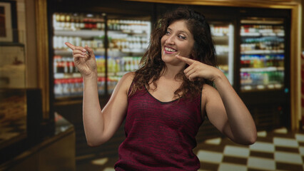 Woman pointing fingers and smiling with raised arms in a restaurant building wearing a sleeveless burgundy shirt; playful confidence.