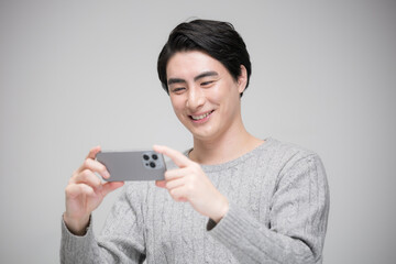 スマホで動画を見るハンサムな笑顔の男性　グレーバック