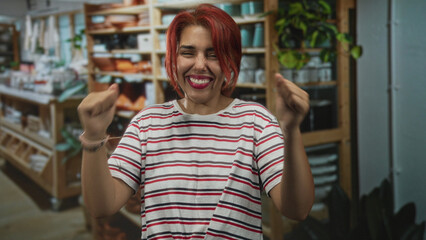 Young hispanic woman smiling with fists raised, dancing with eyes closed in a home decor store; joy...