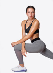 Stretching Young fitness athletic woman wearing grey legging and black top posing looking at camera with determination discipline expression on white background