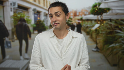 Man claps hands while glancing aside amid urban street planters and building facades near outdoor...